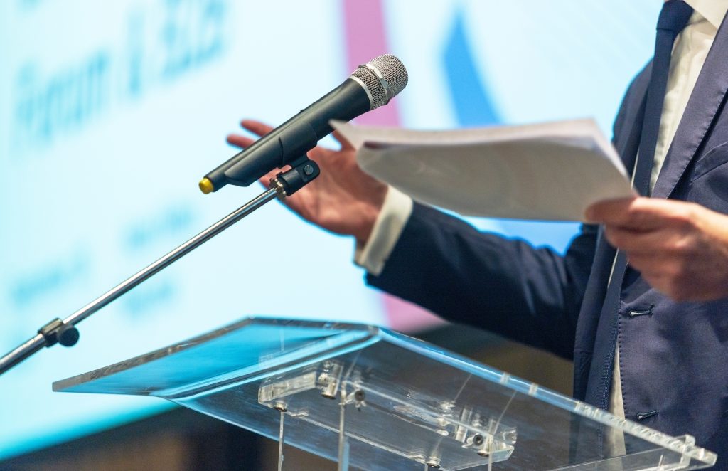 Personne en costume parlant en public, illustrant un témoignage sur les bienfaits du Touch for Health